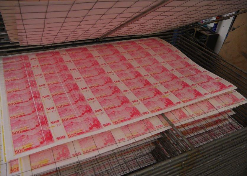 Large sheets of pinkish printed money dry on a multilayered drying rack